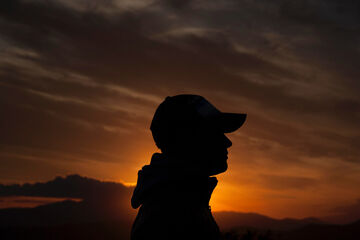 Silhouette of a person wearing a cap against an orange sunset