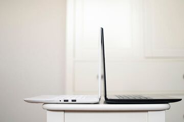 Deux ordinateurs portables, un blanc et un noir, dos à dos sur une petite table blanche
