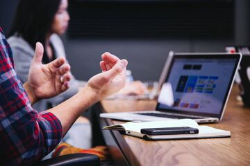 Réunion de travail autour d'une table : une personne gesticule à côté d'un ordinateur portable, d'un carnet et d'un smartphone