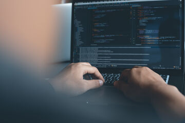 Des mains tapent sur le clavier d'un ordinateur portable affichant du code dans la pénombre